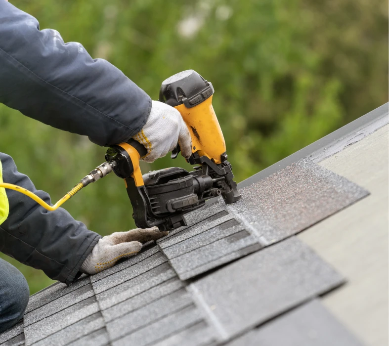 Worker using nail gun on roof shingles